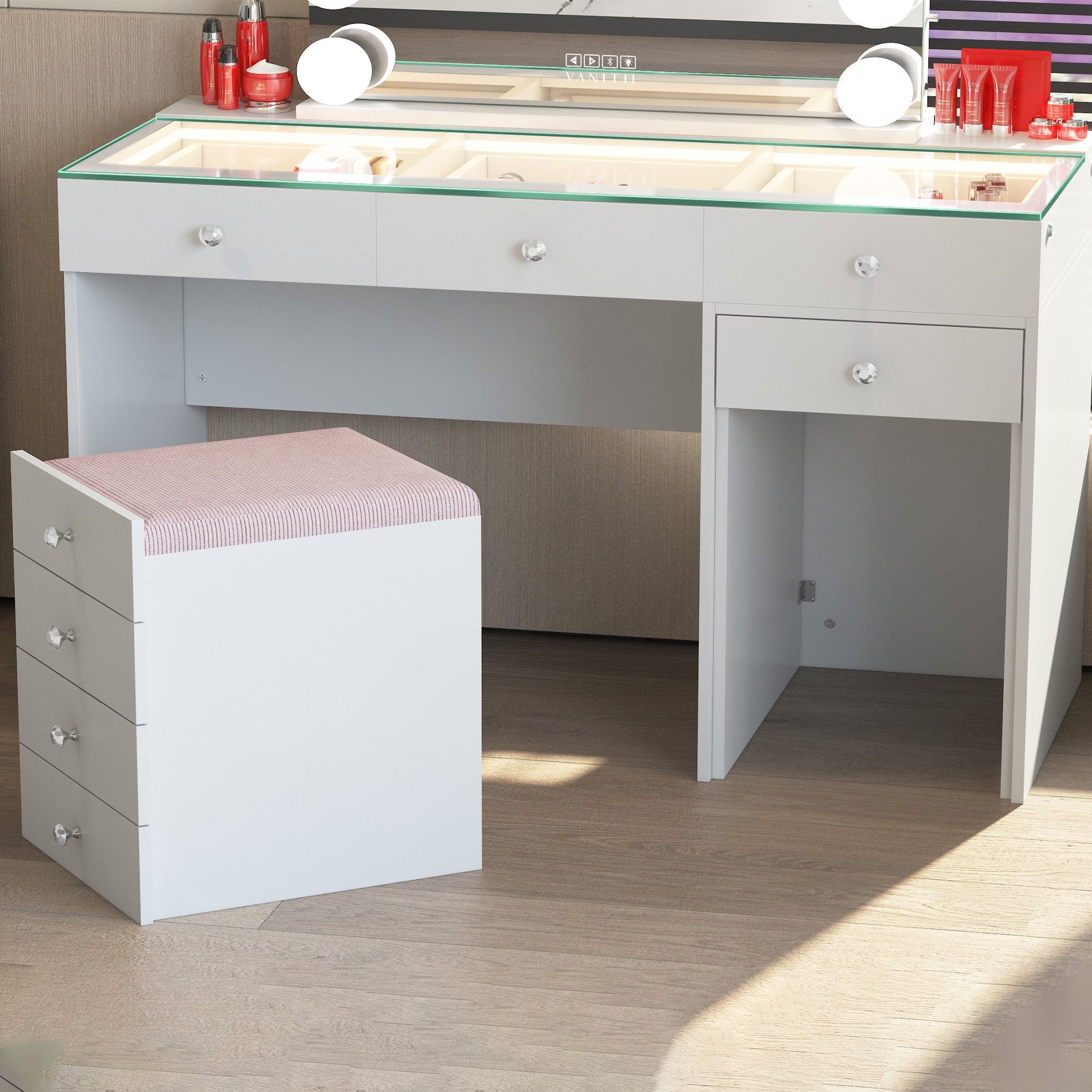 White vanity desk with glass top and pink cushioned stool in a room setting.